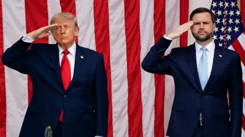 Donald Trump and J D Vance standing next to each other saluting in front of an American flag
