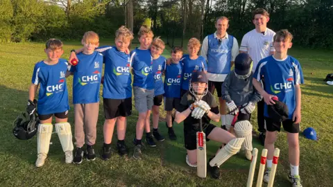 Charlie Webber stands with the players from the West & Middle Cricket Club with their new cricket nets behind them