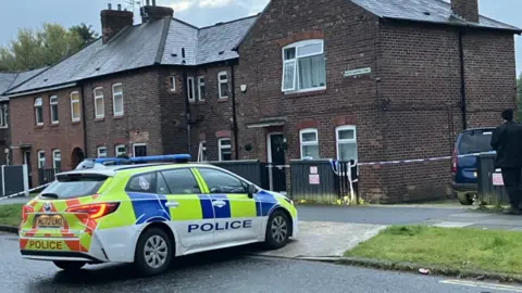 bbc A police car outside the taped-off house where the woman and girl's bodies were found on Monday.