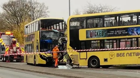 PatKarney A damaged Bee Network bus with a shattered display board behind another Bee Network bus, taped off, where emergency workers pick through debris.