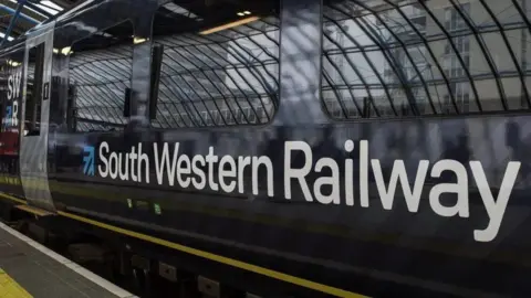 A South Western Railway carriage at a platform. The train is a dark blue with a grey door and the logo is in large white letters.