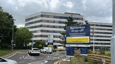 Manchester Airport Large navy blue sign reading 'Barrierless Drop-Off'. 'Remember to pay before midnight tomorrow'.