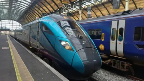 A blue train with TransPennine branding, stationary at a platform in Hull railway station.