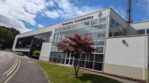 A beige police building with large windows
