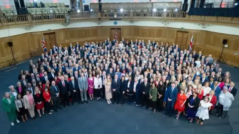 PA Media Semi-circular arrangement of new MPs around Keir Starmer in a large room with blue carpet