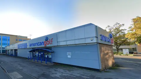 Google A single-storey building, with a tarmacked entrance, with signs on the front and on the right side of the building that say, in lower case lettering "american golf"