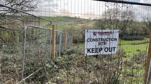 Metal fencing around fields on the Wolborough site with a white sign saying Construction Site - Keep Out