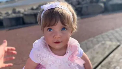 Facebook A little girl in a pink dress with bright blue eyes and dark blonde hair