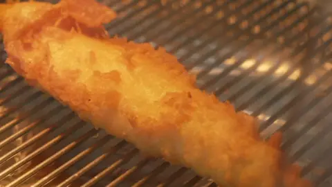 A close-up of battered fish on a fryer.