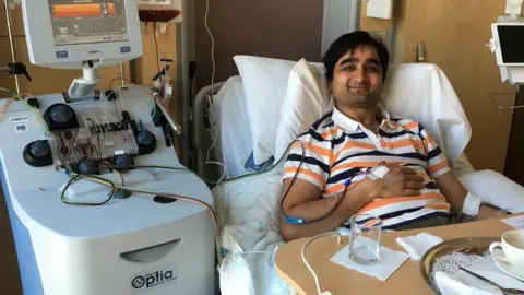 NHS Nirav donating stem cells wearing a stripy shirt in a hospital bed smiling