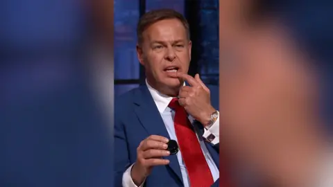 Peter Jones looks confused while he rubs something on his bottom lip