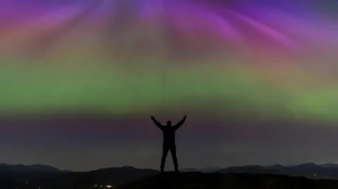 BBC Weather Watchers/Jonny Gios A man on a hilltop with the lights beyond