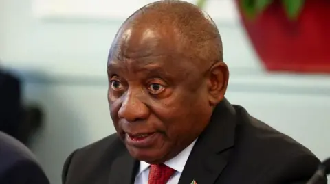 A close-up of President Cyril Ramaphosa wearing a black suit, white shirt and a red-dotted tie. 