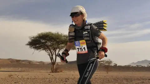 Tower Hill Stables Animal Sanctuary Fiona Oakes wearing her running gear while on a run. She is wearing a white hat and sports gear. She is in a desert landscape. It is cloudy above her.