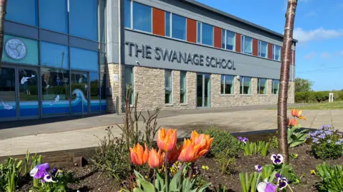 A building made out of brick and windows with orange and purple flowers int he brown flower bed at the front of the building.