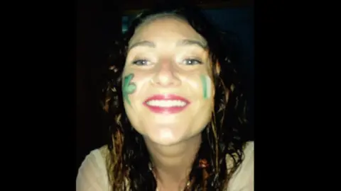 PA Media Danielle McLaughlin smiling at the camera. She has long auburn hair and is wearing face paint on her cheeks depicting a shamrock and an Irish tricolour flag. 