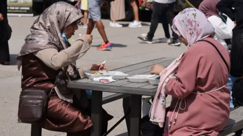 File photo of women wearing headscarves sittng at a table eating from white containers in Toronto, Ontario, Canada, on July 06, 2024.