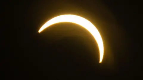 BBC / Jack Valpy A bright crescent of sunlight appears against a black sky as the Moon passes in front of the Sun during a partial solar eclipse.