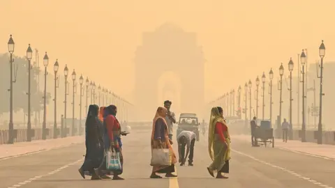 Getty Images People cross the Kartavya Path, near India Gate in Delhi, with the area engulfed in a thick layer of smog in the morning mist of 27 October. 