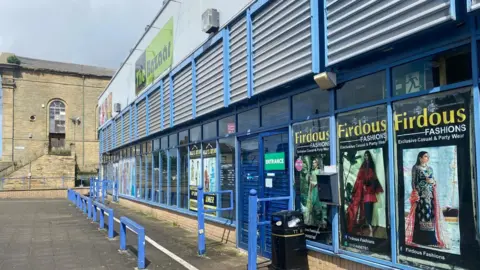 The front of a market building with glass windows and blue frames. The doors are closed.