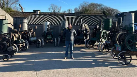BBC/Cathy Killick A man stood in the middle of a semi-circle of vintage engines.