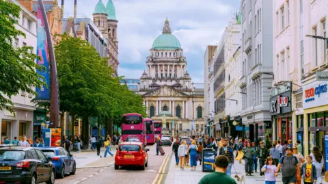 Getty Images Belfast city centre, crowds of people are walking, cars and buses are driving. Belfast City Hall is in the background