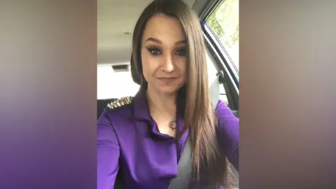 Family picture A young woman in a car with long dark hair wearing a purple top looks confidently to camera.
