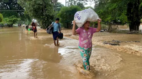 La gente del EPA lleva sus pertenencias mientras camina por las aguas de la inundación en Pyinmana, Naypyidaw, Myanmar, el 13 de septiembre de 2024.