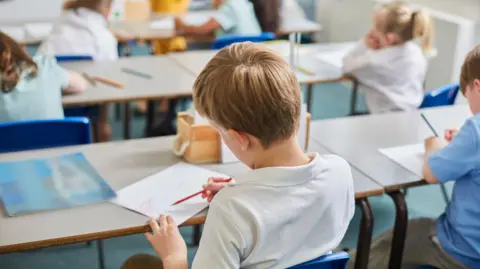 Getty Images School boy sitting at a desk writing on a piece of paper