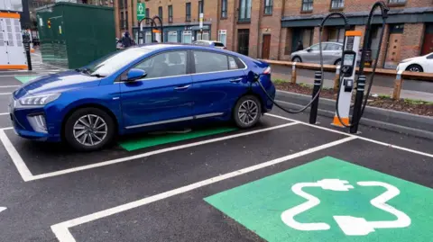 Getty Images Blue car in a car park and being charged at a public charging point