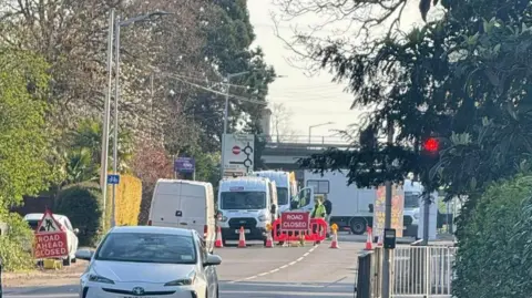 Kirsty Knight Red road closed signs with some cars seen driving on a grey tarmac road. 