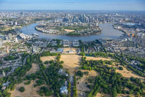 jasonhawkes.com Aerial shot from above the yellow grass of Greenwich Park towards the Isle of Dogs with the River Thames going around it