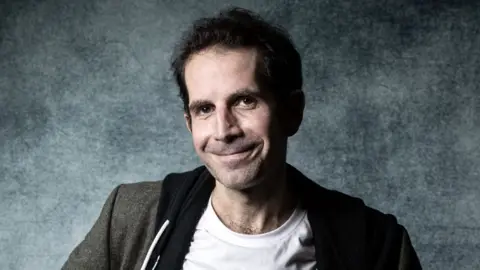 Getty Images Julien Berjeaut smiling at the camera. He has short dark hair and is wearing a white t-shirt with a black hoodie and then grey jacket over the top.