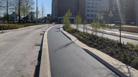 A freshly tarmacked cycle path alongside an existing road through Swindon town centre.
