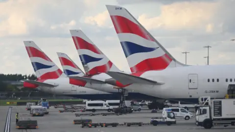 BBC The tailfins of four British Airways planes on the tarmac at Heathrow Airport. The planes are white with a stylised part of the union jack on their tailfins