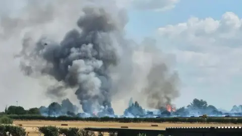 Field with smoke in and blue skies behind