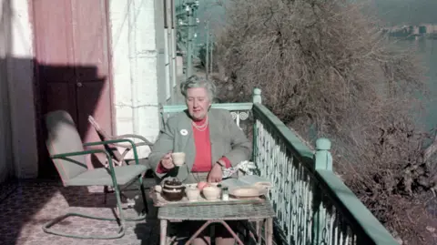 Christie Archive Trust A coloured archive image of Agatha Christie drinking tea on a balcony in Baghdad in about 1950. It is a sunny day.