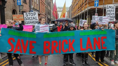 Campaigners march through Brick Lane carrying a large "Save Brick Lane" banner and placards opposing plans for data centres and calling for more homes.