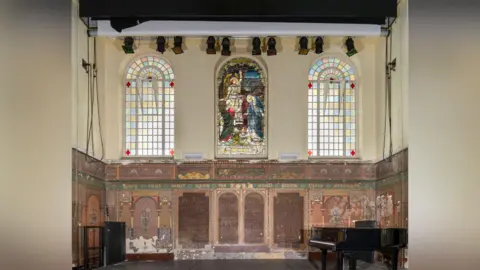 Historic England The chancel of a church. There is also a black piano and stained glass window. 