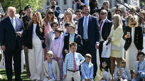 Getty Images Crowd of people, many children, dressed in beige and pastels, with Trump standing on one side in dark suit