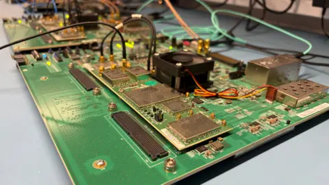 Ben Schofield/BBC A close-up shot of a circuit board, with another immediately behind it. There are several components mounted onto the board and wires coming in and out of them. The shot is taken with the bottom right hand corner of the board pointed towards the lens.