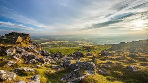 A landscape image taken on Dartmoor showing a cloudy sky with the sun rising. 