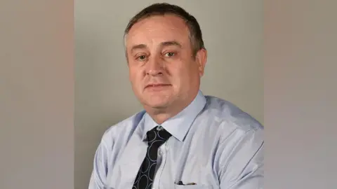 St Helens Borough Council David Hawley has short dark hair and is wearing a light blue shirt with a dark blue tie