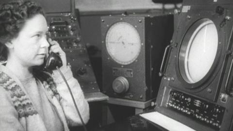 Woman holds a telephone reciever, while looking at an aircraft radar
