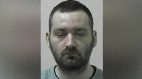 Mugshot of Jordan Reilly. He has his eyes half closed and has short dark hair and a beard.