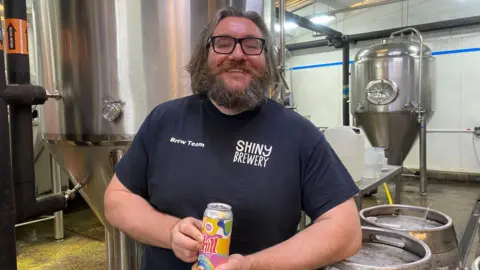 Chris Butcher holding a can of 0.3% beer inside Shiny Brewery in Derby