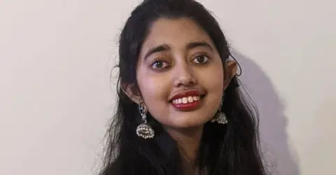 Family Sudiksha Thirumalesh, who has long dark hair, dark eyes and is wearing dangly earrings smiles at the camera