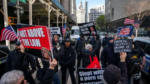 Reuters Protests hold signs reading "not above the law" and the "the emperor has no dough"  as police stop them from approaching the Manhattan criminal court