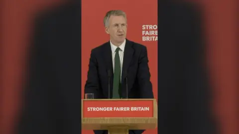 UK Defence secretary Dan Jarvis speaking from podium in front of red background