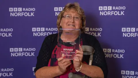 Alistair Beavis/BBC Diane Boothby wearing a black and red dress holding her Make a Difference glass award.